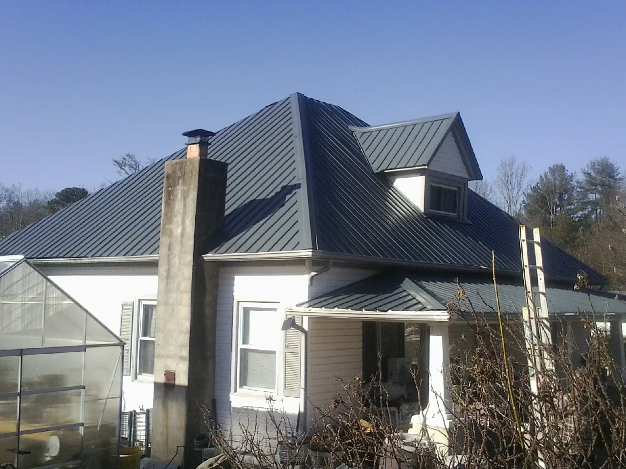 Dark blue standing seam metal roof on a white farmhouse with dormer — Slate & Tile Roof Repair by Roofing Brothers in Vida