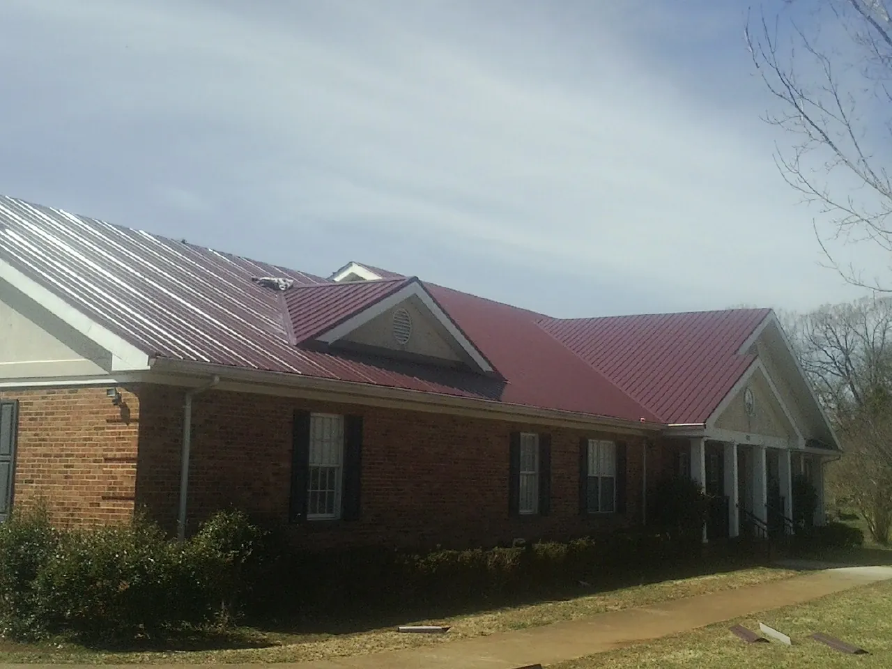 Red metal roof with gabled entries on a long brick building, from a Hail Damage Roof Repair job in Vida