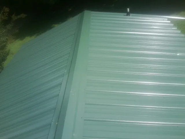 New green metal panels meeting at the ridge of a roof — Flat Roof Repair work by our crew in Vida