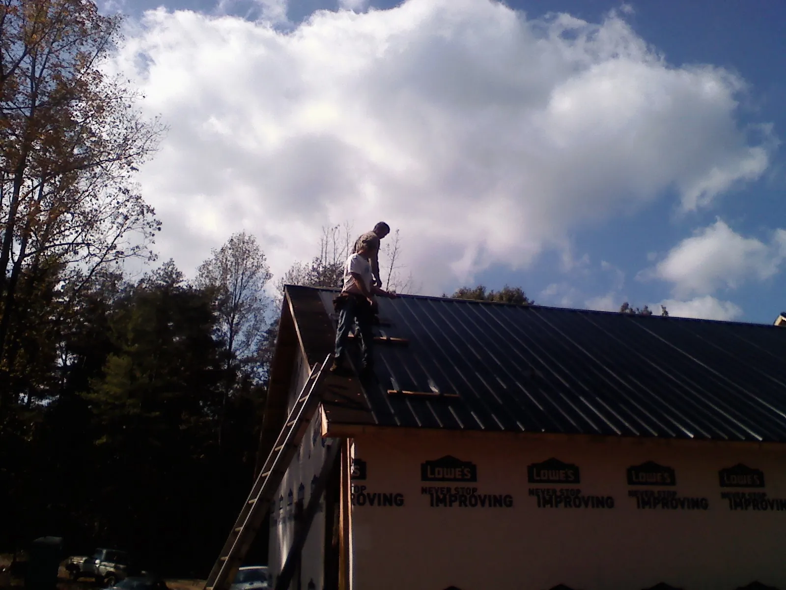 Roofer fastening dark metal panels high against a cloudy sky, from a Roof Inspection job in Vida