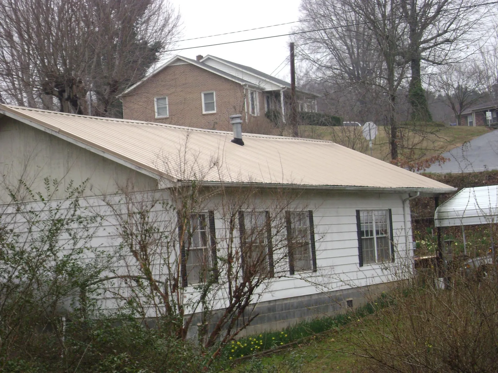Tan metal roof on a white sided house set into a hillside — Commercial Roofing by Roofing Brothers in Vida