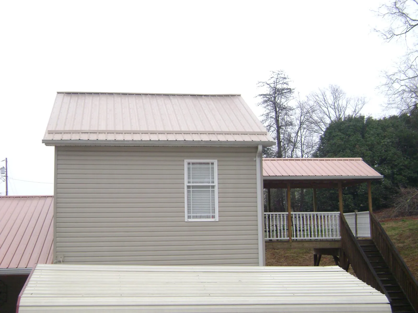 Tan metal roofs on a two story addition and attached porch, from a Roof Replacement job in Vida